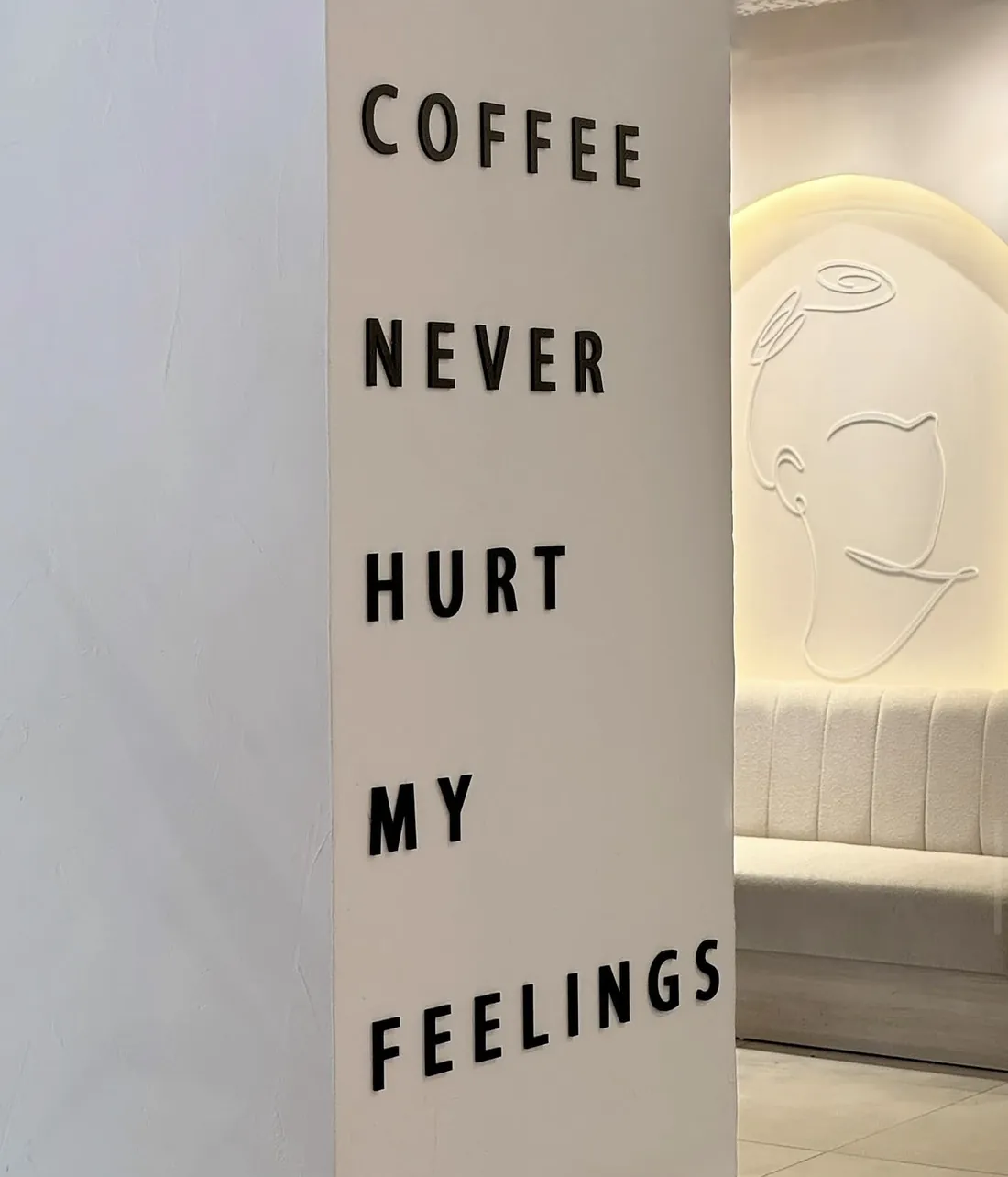 Lettering “Coffee never hurt my feelings” on the wall, a bench behind it